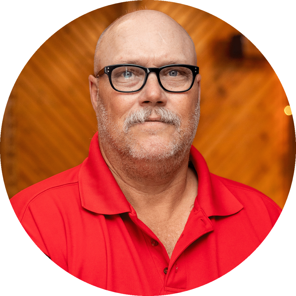 man with black glasses and gray mustache wearing a red polo shirt.