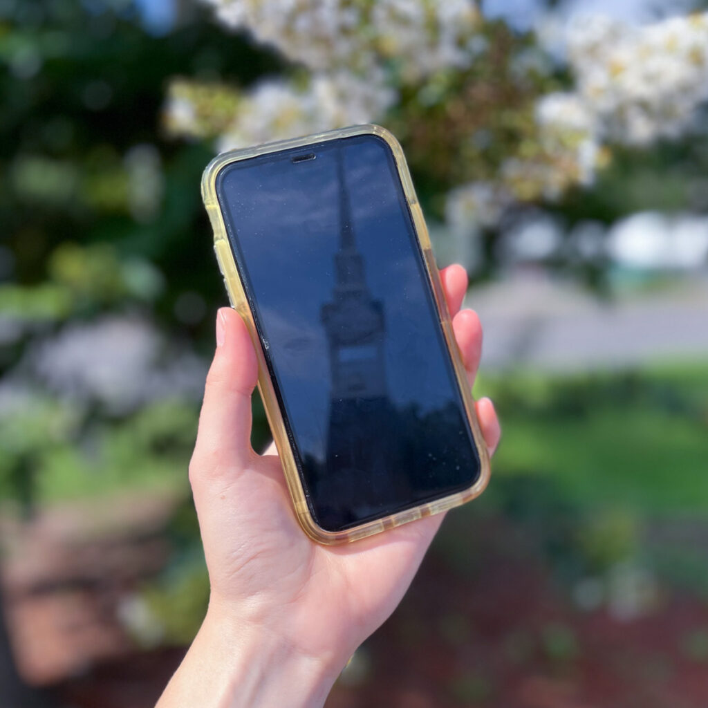 hand holding a phone reflecting a church steeple.