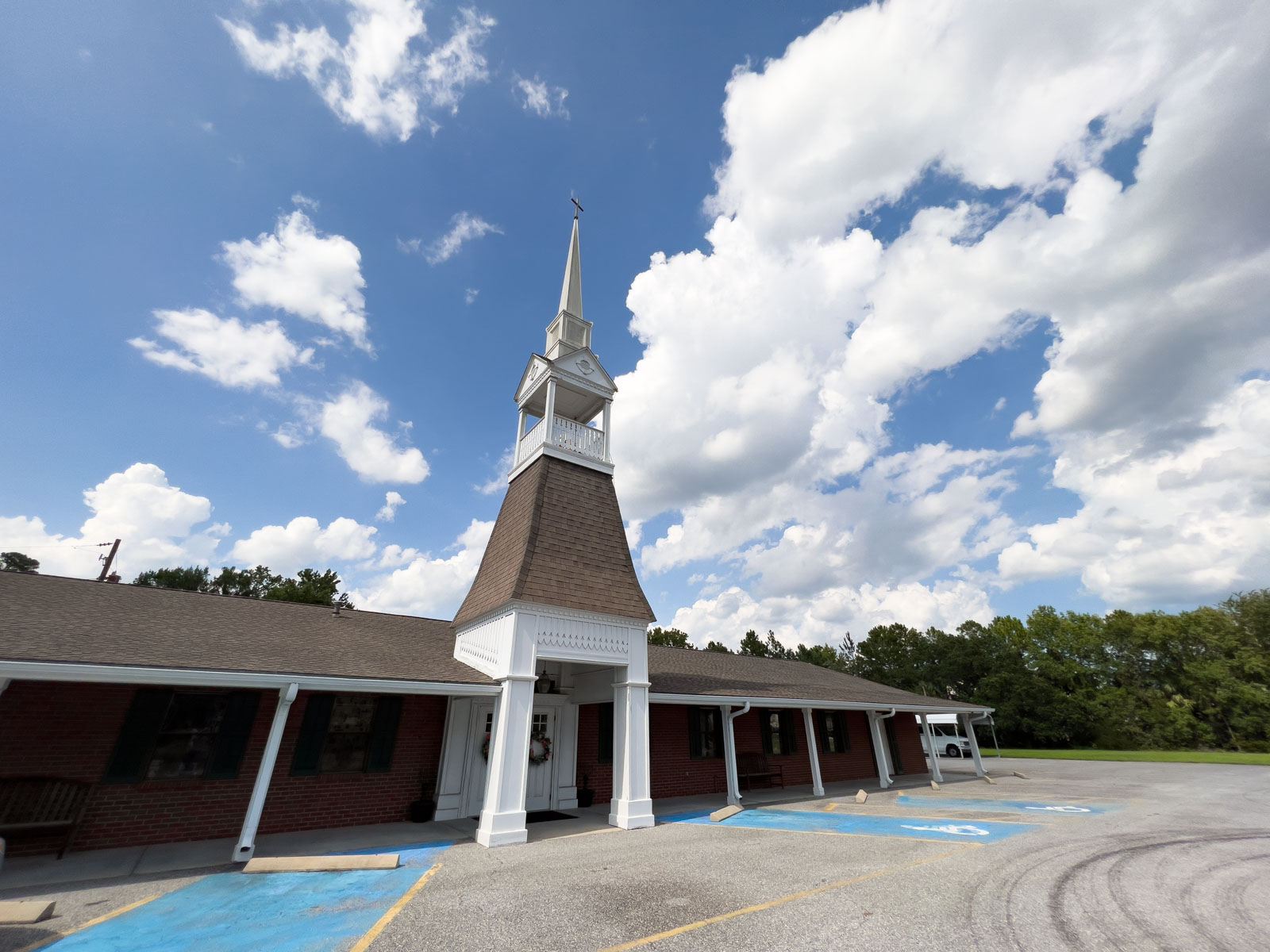 exterior of a brick church with a white steeple on a sunny day.