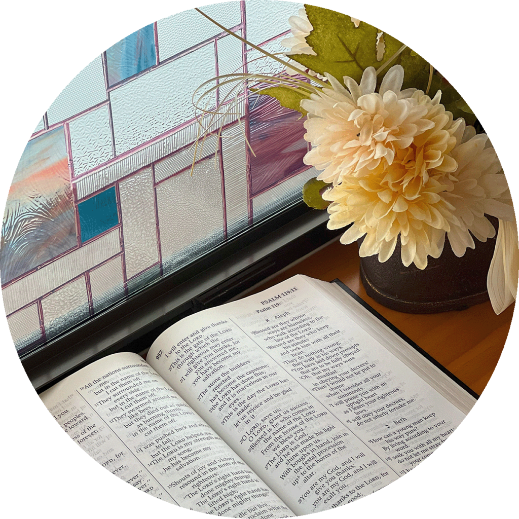 Bible in the window of a church near a small flower arrangement.