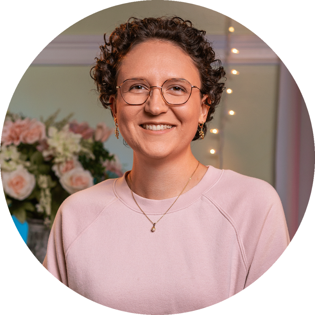 smiling younger woman with short, curly brown hair and glasses.