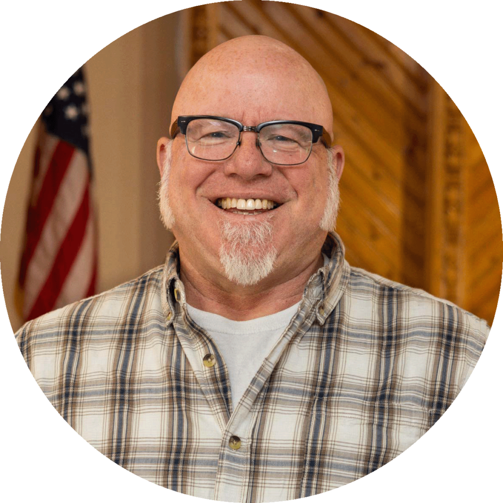 smiling man with glasses, white beard and sideburns, and a plaid shirt.